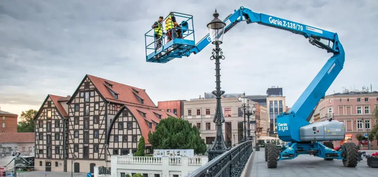 Pracownicy na podnośniku koszowym Genie Z-135/70 naprawiają latarnię. Zastanawiasz się, ile kosztuje wynajem podnośnika koszowego?