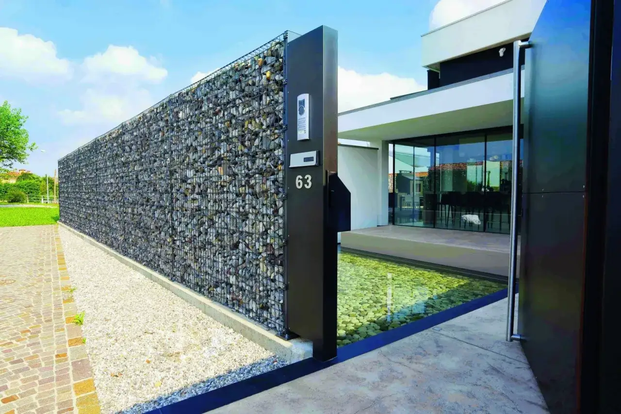 Nowoczesne ogrodzenie na taras z kamienia w gabionach, z wbudowanym domofonem i numerem 63.