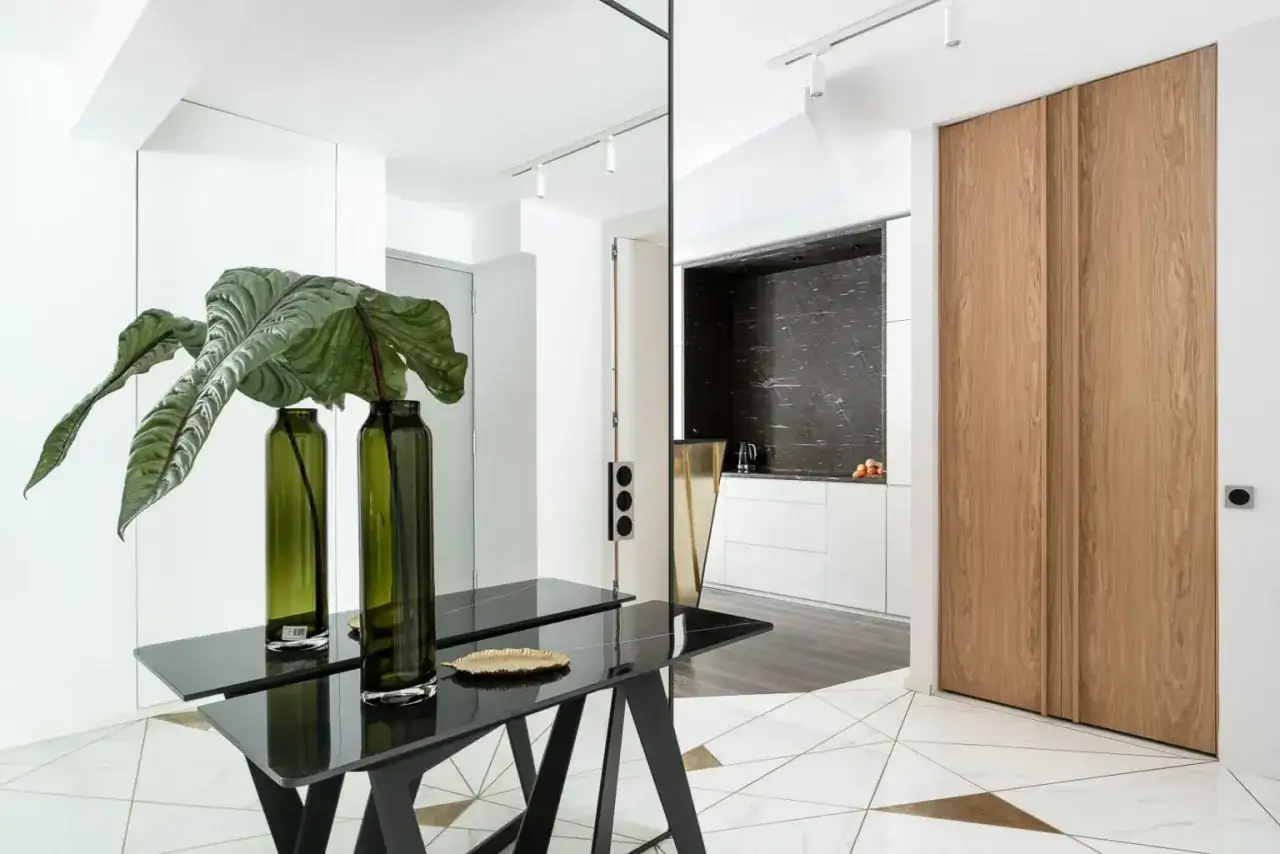 Nowoczesny przedpokój z czarnym stolikiem, zielonymi wazonami z rośliną i drewnianymi drzwiami. Świetny pomysł na ścianę w przedpokoju.