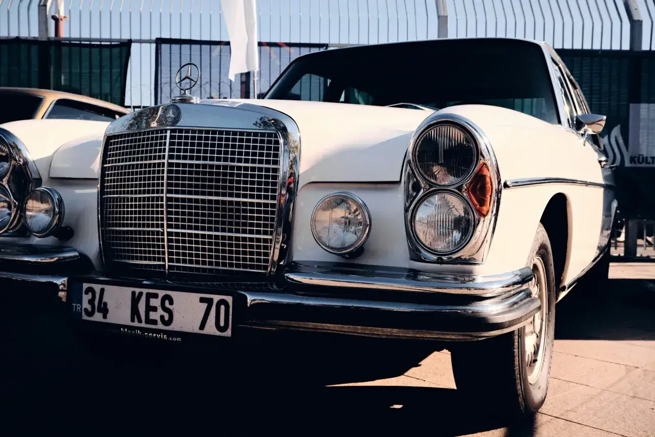 Biały, zabytkowy Mercedes z chromowanym grillem i podw&oacute;jnymi reflektorami. Te zdjęcia z samochodem to prawdziwa podr&oacute;ż w czasie.