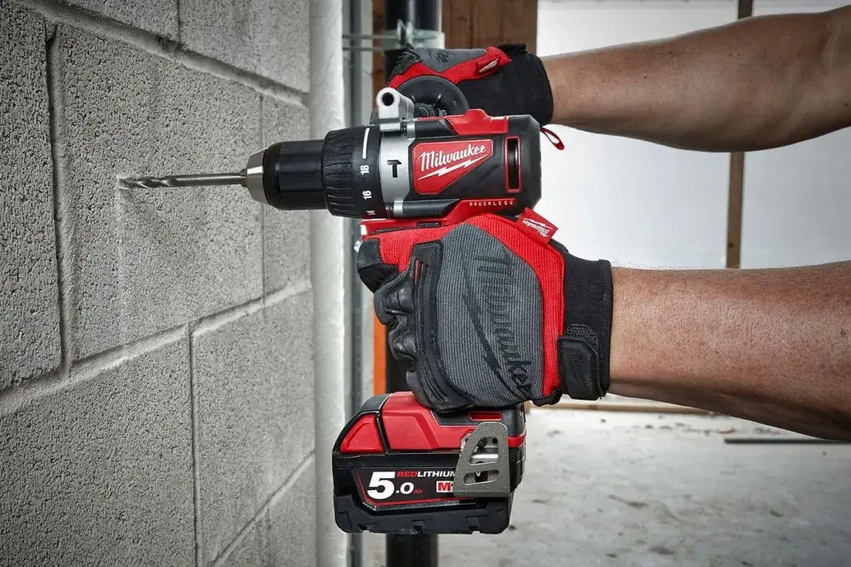 Ręce w rękawicach trzymają wkrętarkę Milwaukee, kt&oacute;ra wierci w betonowej ścianie. Tak, wkrętarka można wiercić w ścianie.