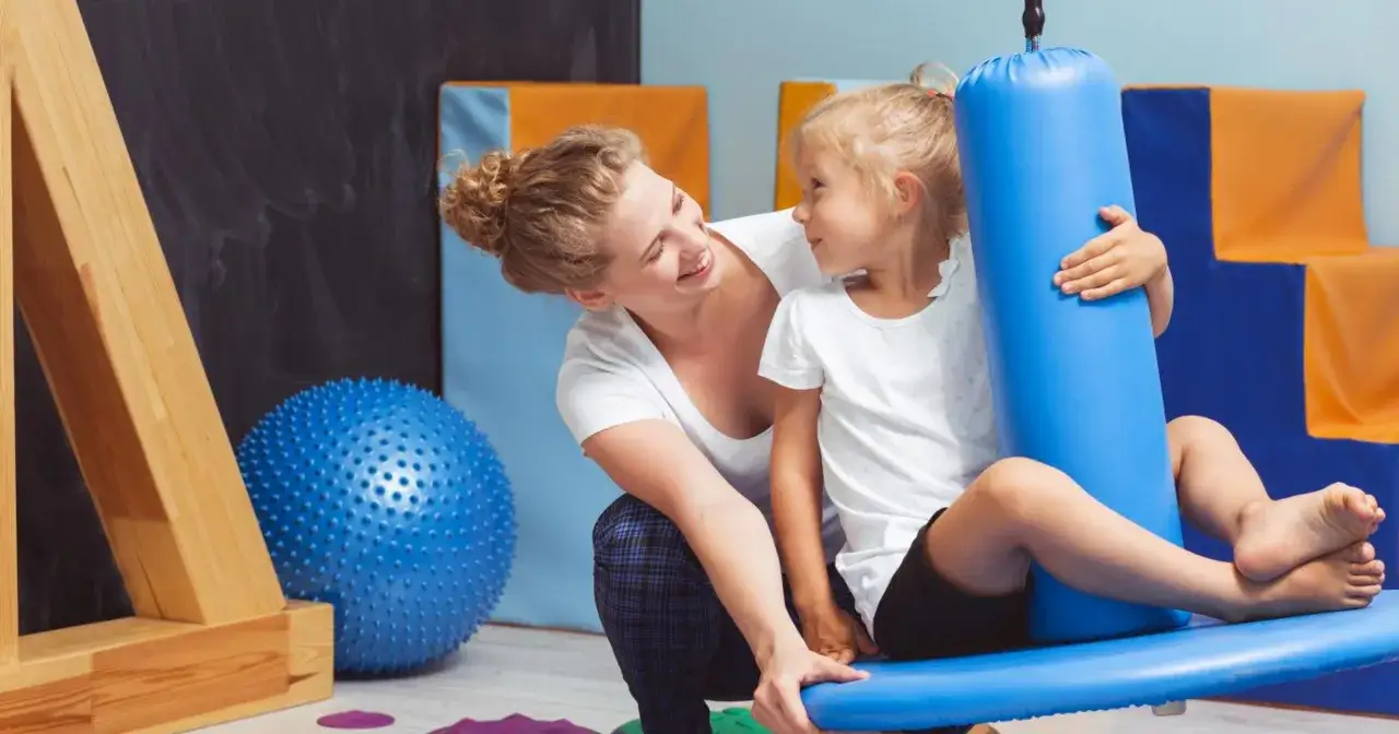 dziecko na huśtawce terapeutycznej, rodzic bawiący się z dzieckiem w domu