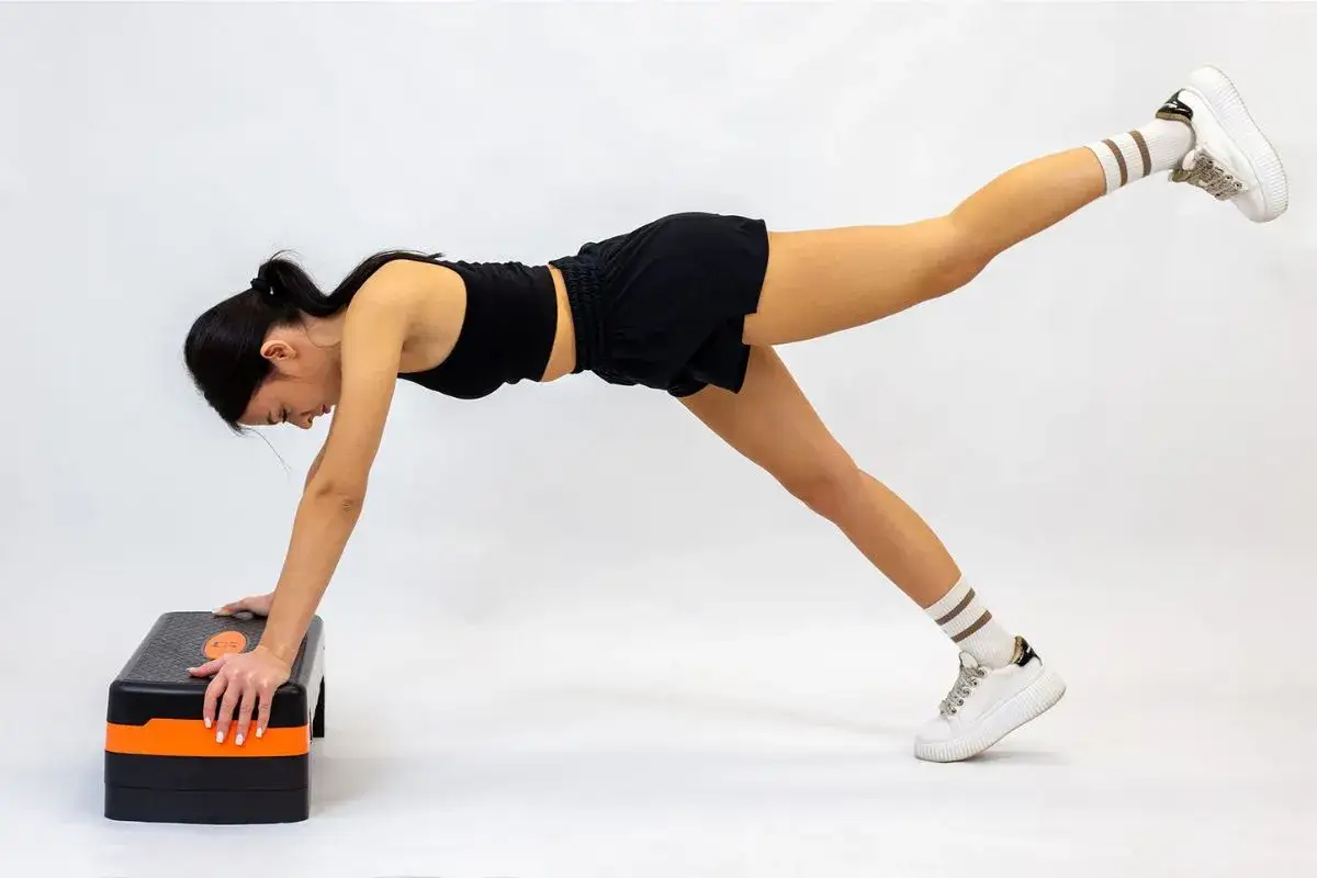Kobieta wykonuje ćwiczenia na stepperze, unosząc jedną nogę w tył.