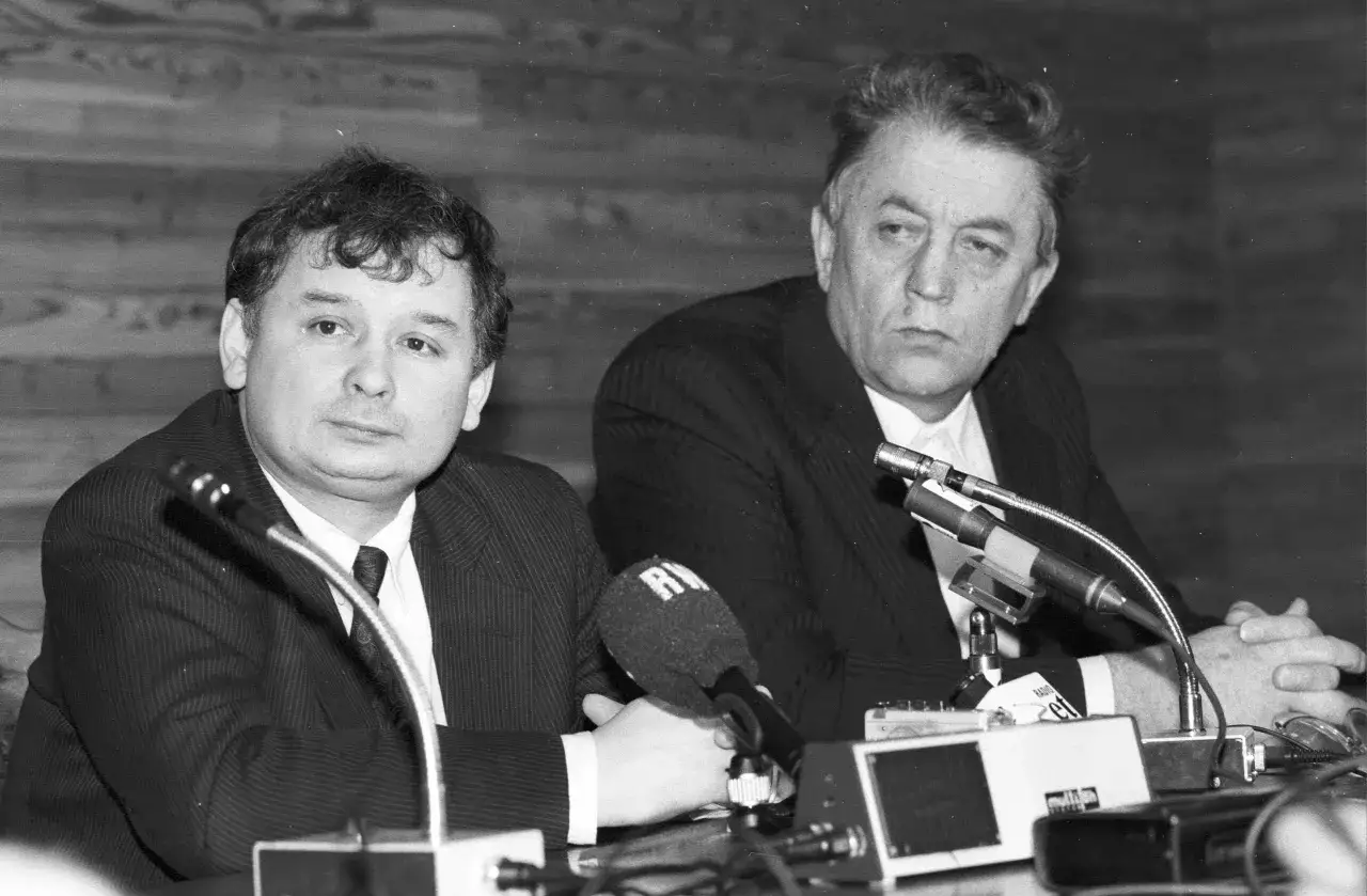 Dwóch mężczyzn przy mikrofonach. Jeden z nich, z charakterystyczną fryzurą, to Lech Kaczyński, który wraz z bratem Jarosławem założył PiS.