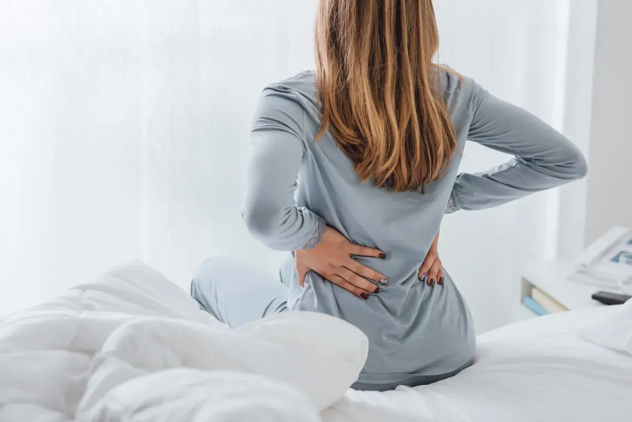 Kobieta z b&oacute;lem plec&oacute;w zastanawia się, do jakiego lekarza z osteoporozą się udać.