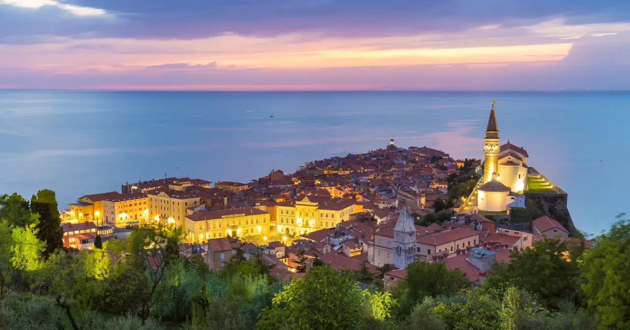 Widok na miasteczko na wzgórzu nad morzem o zachodzie słońca. Odpowiedź na pytanie: czy Słowenia ma dostęp do morza? Tak, ma.