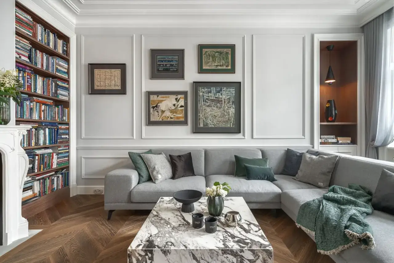 Elegancki salon z szarą sofą, marmurowym stolikiem i regałem z książkami. Sztukateria jak rozplanować? Zobacz inspiracje na ścianach.
