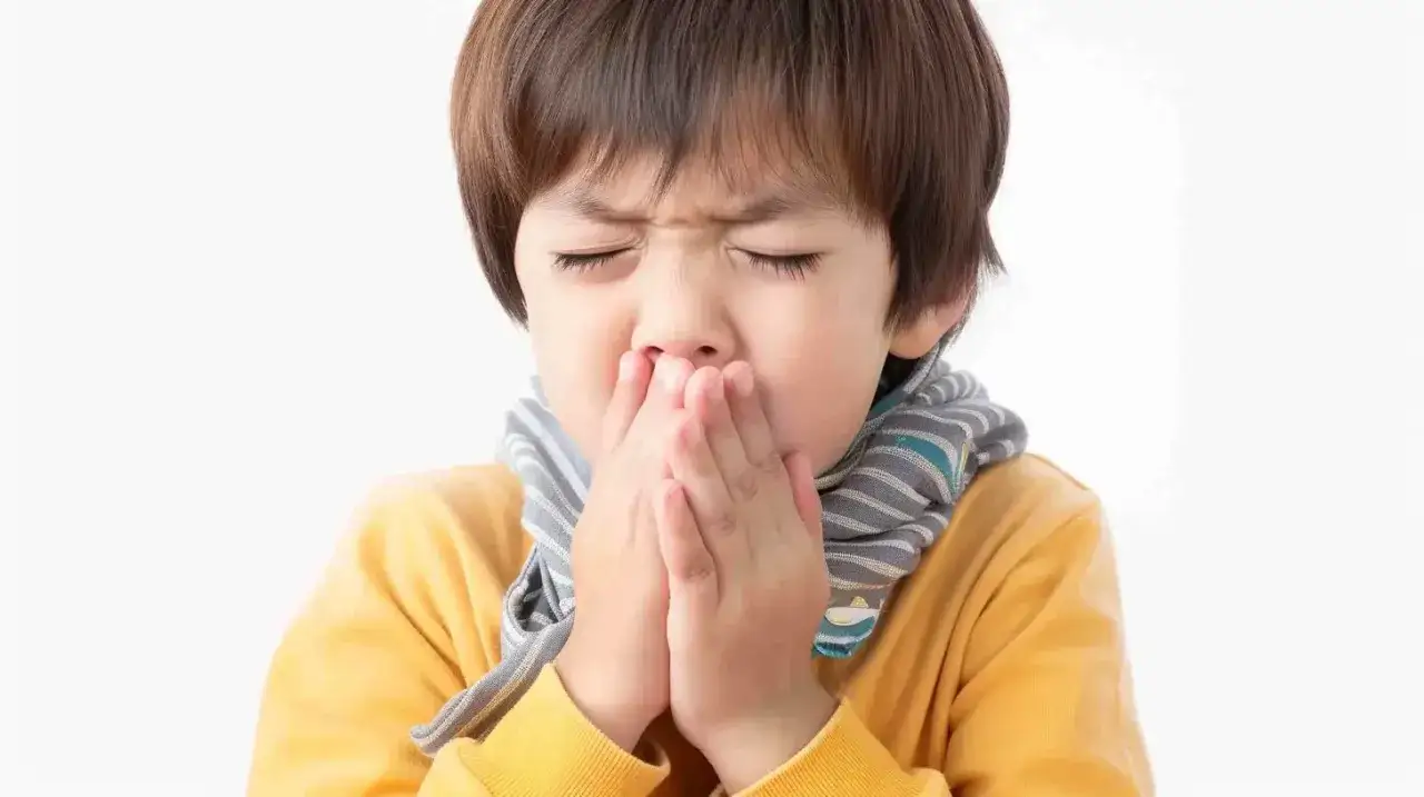 Chłopiec z zasłoniętymi ustami i nosem, z zamkniętymi oczami, w ż&oacute;łtej bluzie i szaliku. Wygląda na to, że ma mokry kaszel u dziecka.