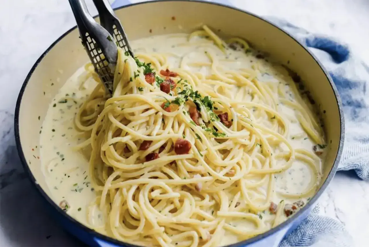 Kremowe spaghetti carbonara ze śmietaną i chrupiącym boczkiem, posypane natką pietruszki. Pyszne danie w niebieskim naczyniu.