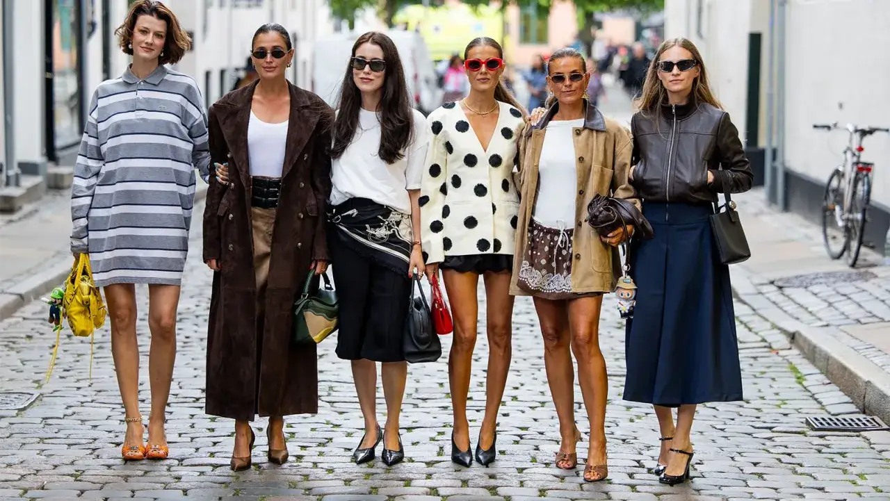 Sześć kobiet prezentuje stylowe, skandynawskie marki odzieżowe na brukowanej ulicy.