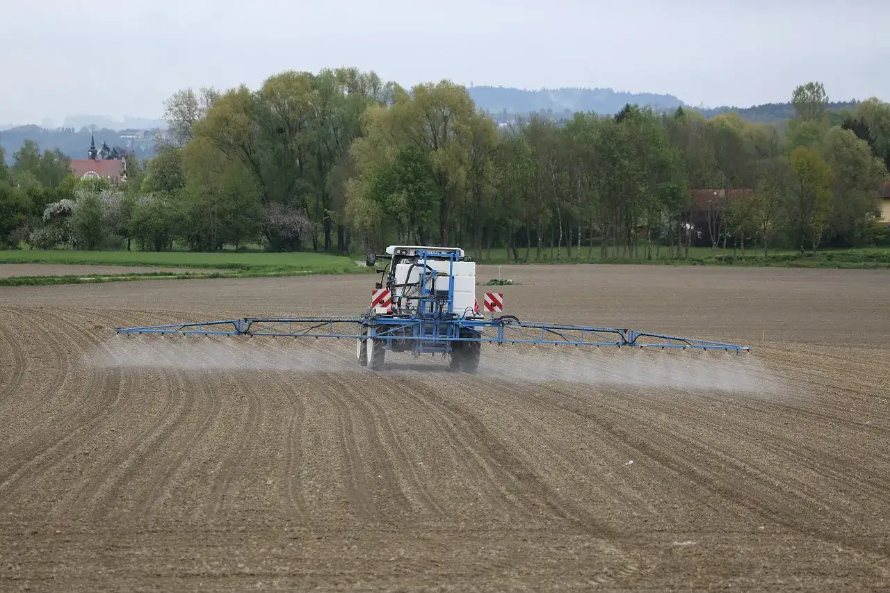 Traktor opryskuje pole, rozprowadzając środek, który może być glifosatem. To pytanie o to, czym jest glifosat, pojawia się w kontekście rolnictwa.