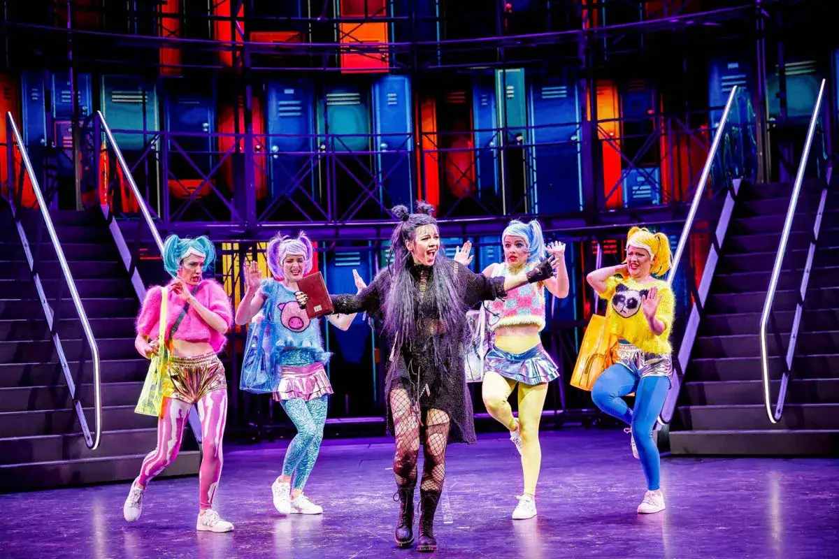 Pięć artystek w kolorowych strojach na scenie, w tle niebieskie szafki. To scena z musicalu 