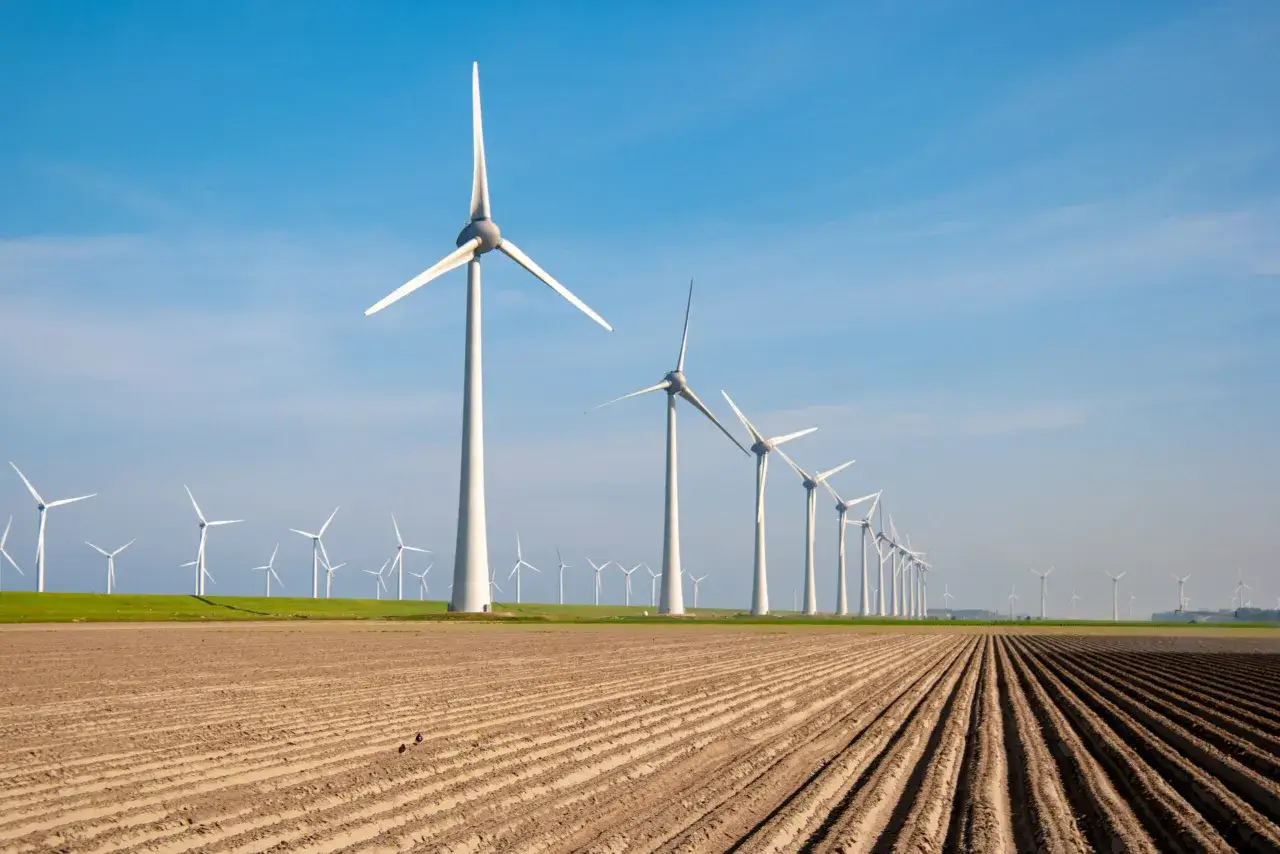 Rząd białych turbin wiatrowych, mała elektrownia wiatrowa, na tle błękitnego nieba nad zaoranym polem.