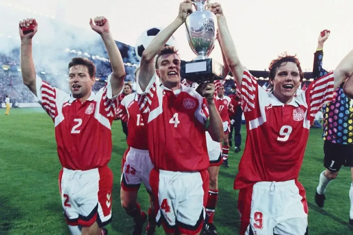 Radość piłkarzy Danii z lat 90. po zdobyciu pucharu. Świętują zwycięstwo, unosząc trofeum nad głowami.