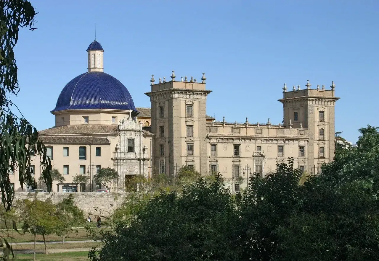 Imponujący budynek z niebieską kopułą, część muzeum sztuk pięknych w Walencji, otoczony zielenią.