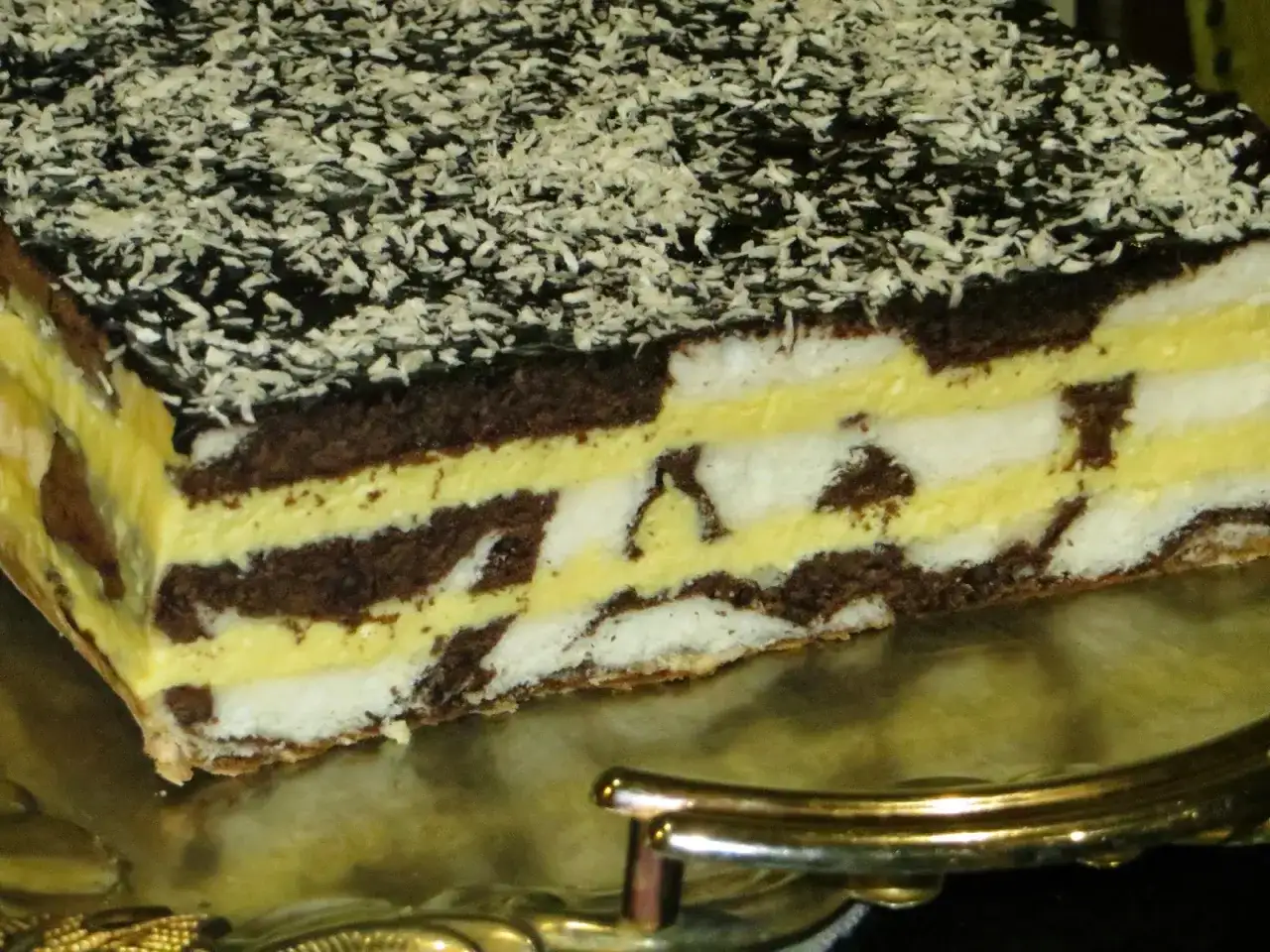 Warstwowe ciasto z serem, przełożone kremem i czekoladą, posypane wiórkami kokosowymi.