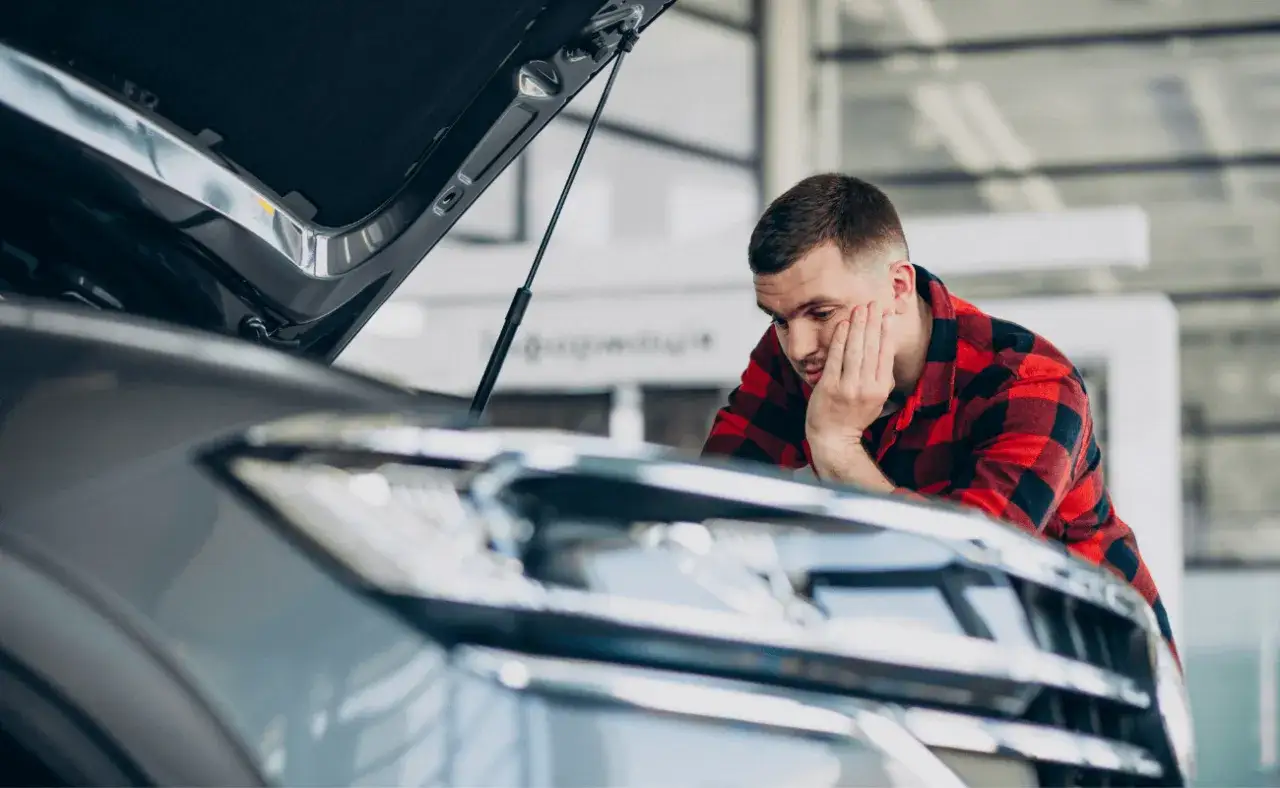 Mężczyzna w kratę sprawdza auto po naprawie bezgotówkowej. Zamyślony, opiera głowę na dłoni, patrząc na silnik.
