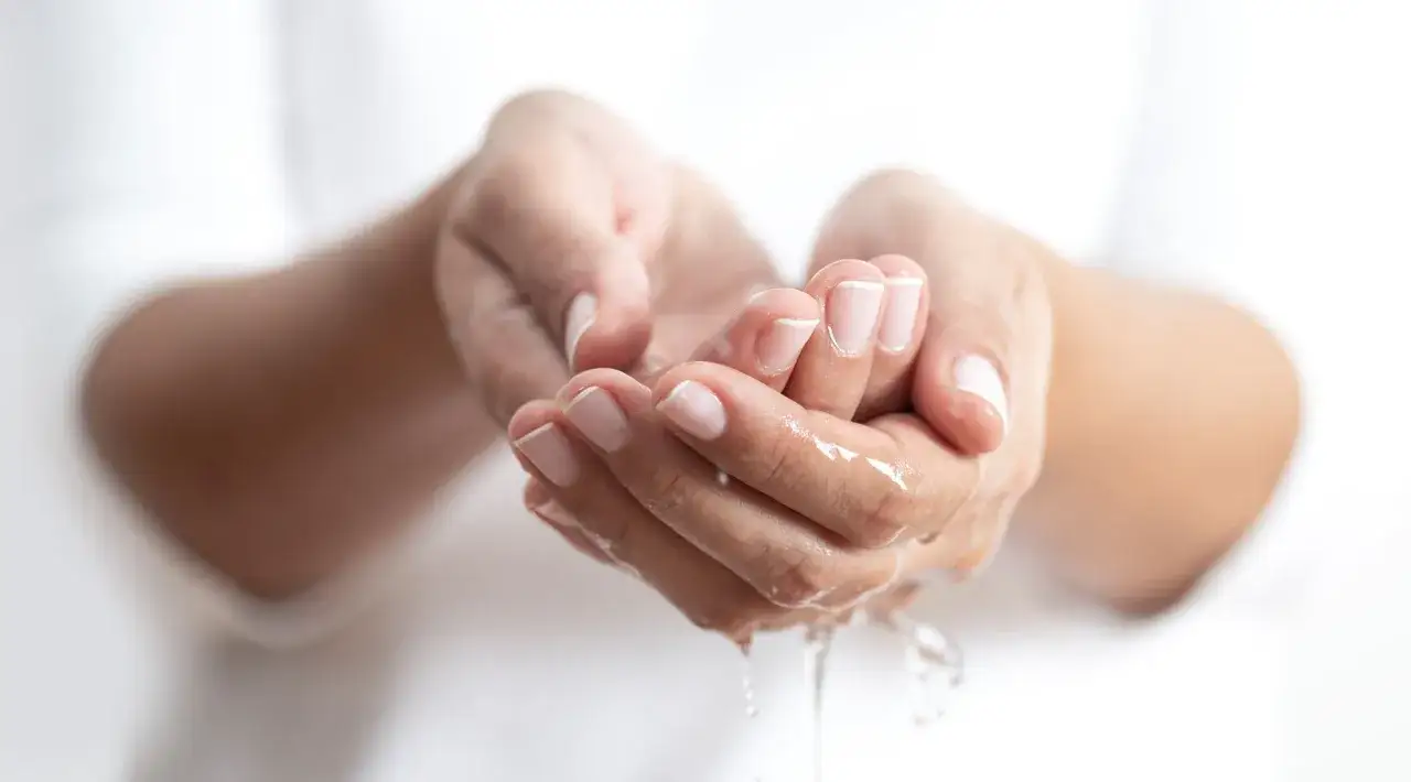 Dłonie z zadbanymi paznokciami, na których widać delikatne rozdwajające się paznokcie, obmywane wodą.