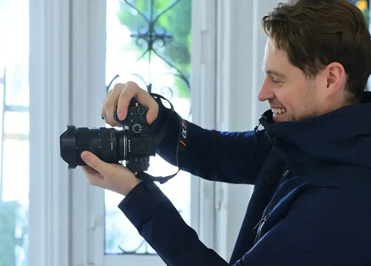 Uśmiechnięty mężczyzna z aparatem w rękach, jakby uczył się na kursie fotografii.