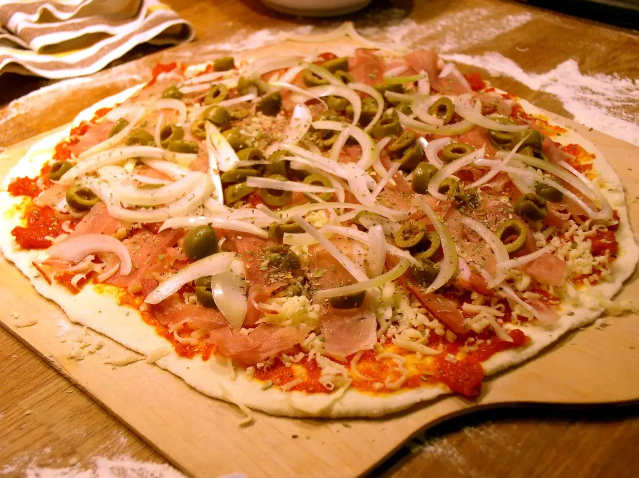 Pyszna pizza rzymska przepis: cienkie ciasto, sos pomidorowy, ser, szynka, oliwki i cebula.