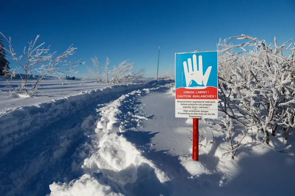 Znak ostrzega przed lawinami. Śnieżny szlak prowadzi przez zimowy krajobraz, gdzie stopnie zagrożenia lawinowego mogą być wysokie.