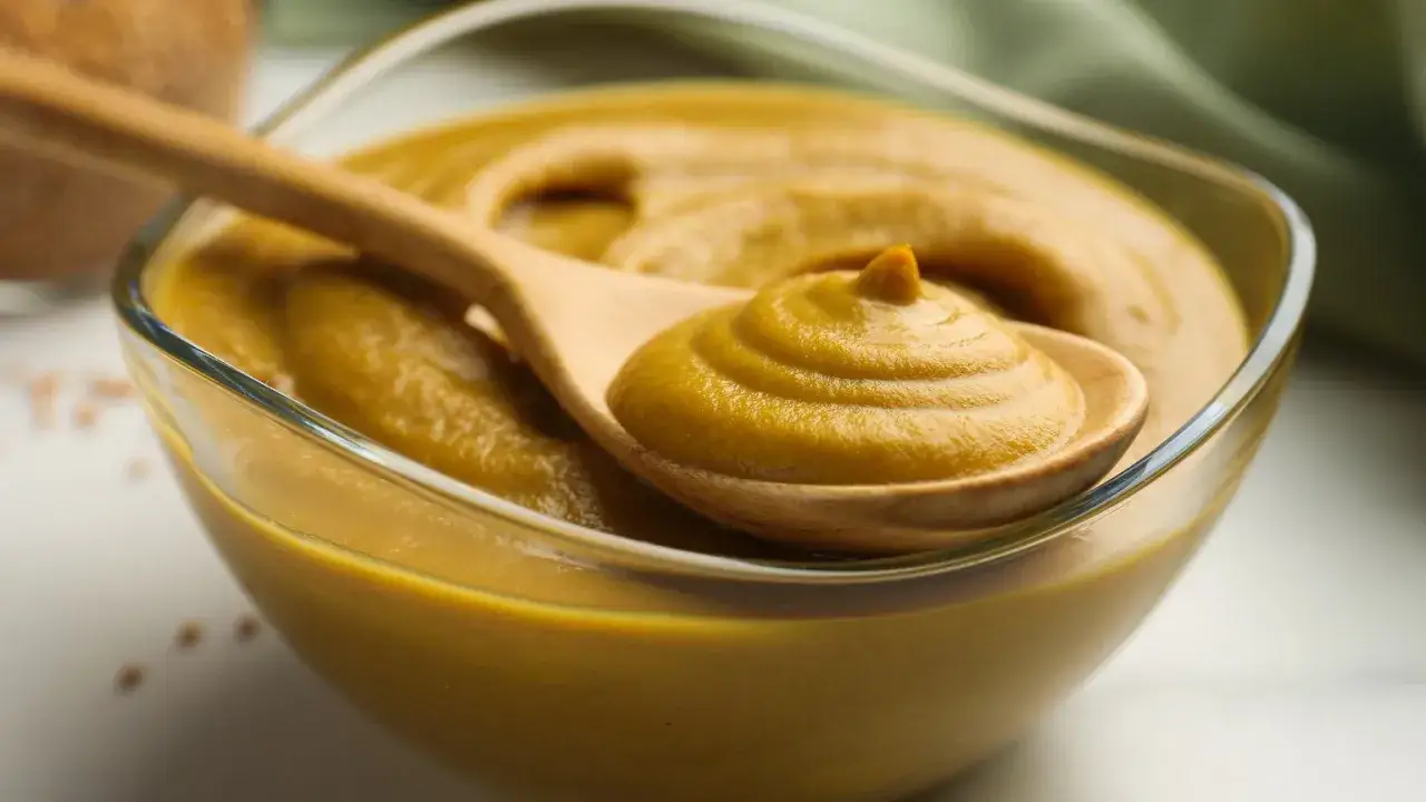 Gęsty, złocisty sos musztardowy na drewnianej łyżce, gotowy do podania.