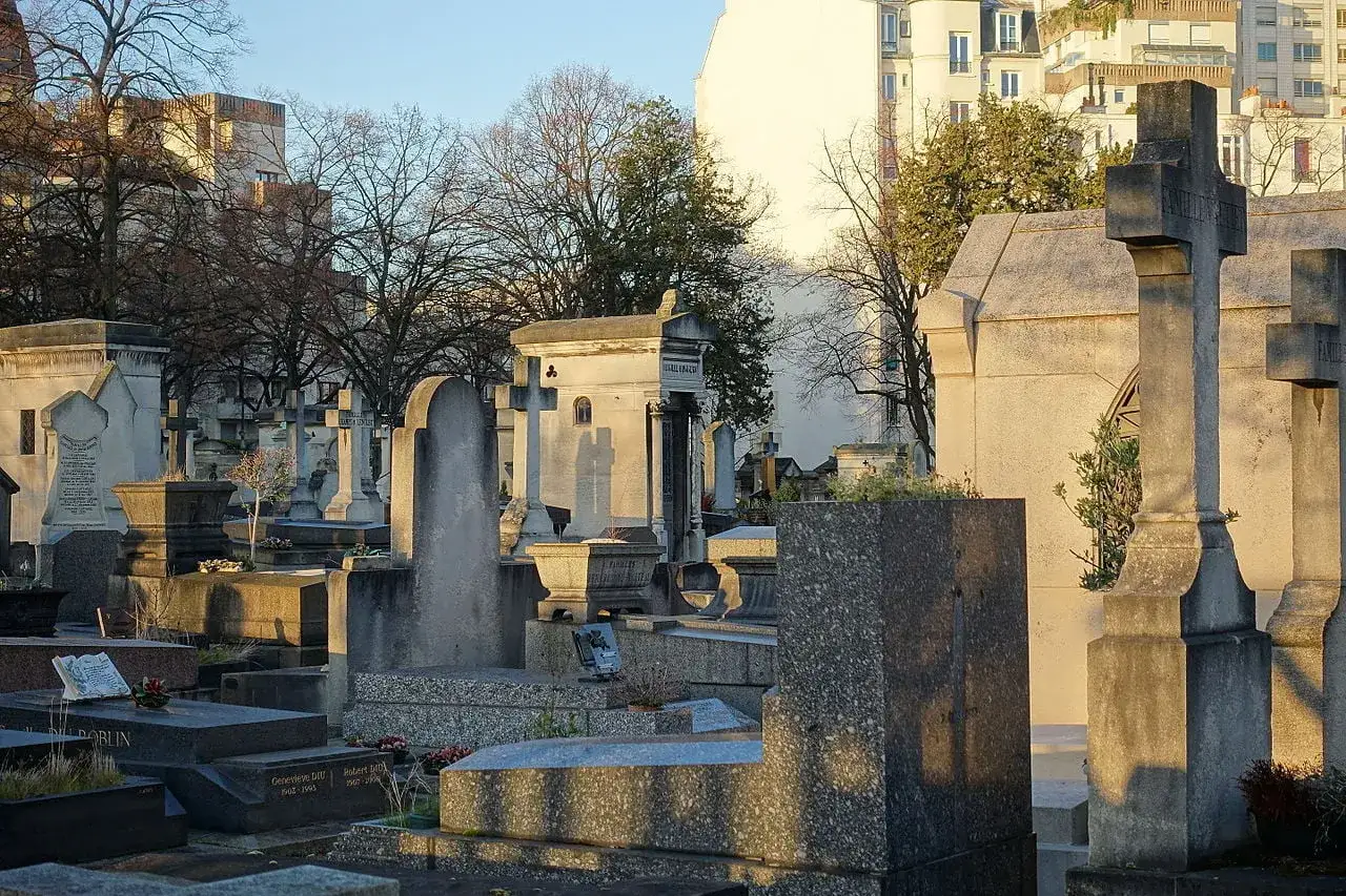 Nagrobki i mauzolea na cmentarzu w 14 dzielnicy Paryża, oświetlone ciepłym, popołudniowym słońcem.