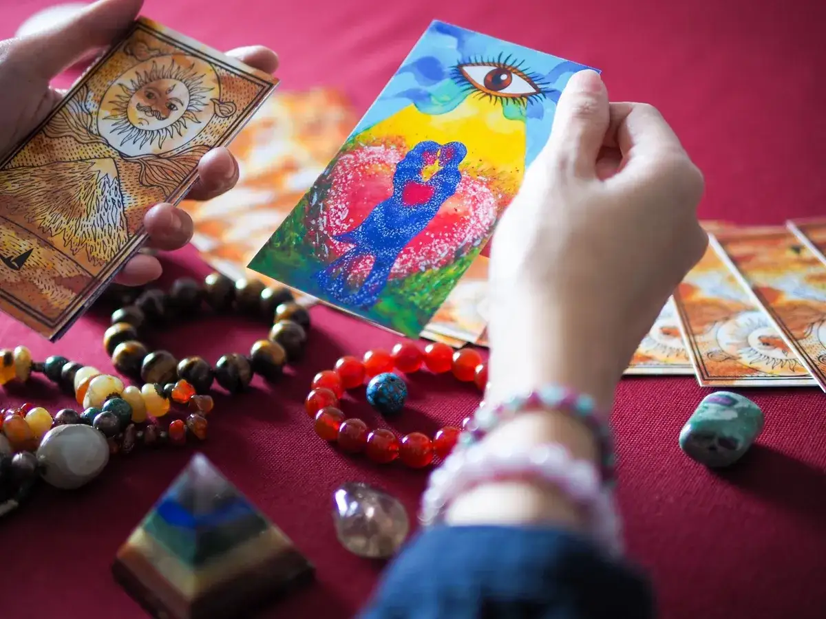 Ręce trzymają karty tarota, przygotowując horoskop panna codzienny. Wokół rozsypane kamienie i bransoletki.