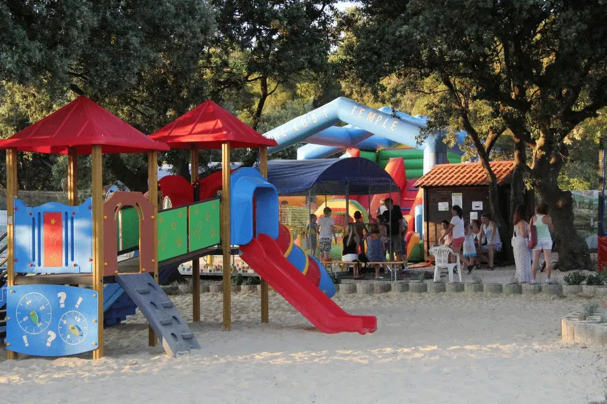Kolorowy plac zabaw i dmuchany zamek tworzą idealne miejsce na **camping dla dzieci**. Dzieci bawią się w piasku i na zjeżdżalniach.