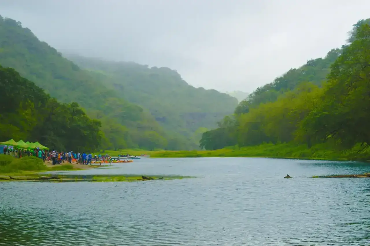 Zielone wzgórza otaczają spokojną rzekę, gdzie ludzie przygotowują się do rejsu. To idealne miejsce, by dowiedzieć się, kiedy najlepiej lecieć do Omanu, by cieszyć się takimi widokami.