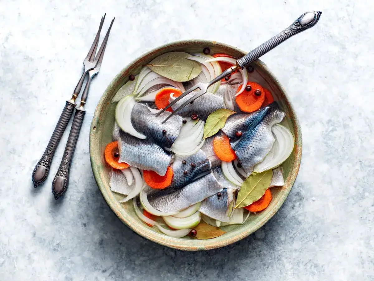 Śledzie w zalewie octowej z cebulą i marchewką, gotowe do podania. Obok widelce do śledzi.