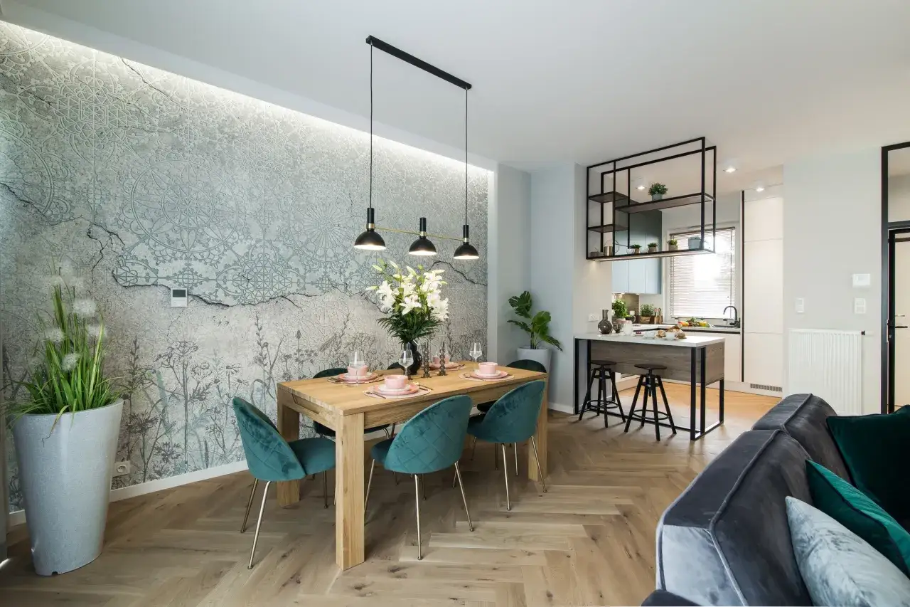 Elegancka sciana glamour w salonie z subtelnym wzorem i oświetleniem. Drewniany stół z zielonymi krzesłami, w tle nowoczesna kuchnia.