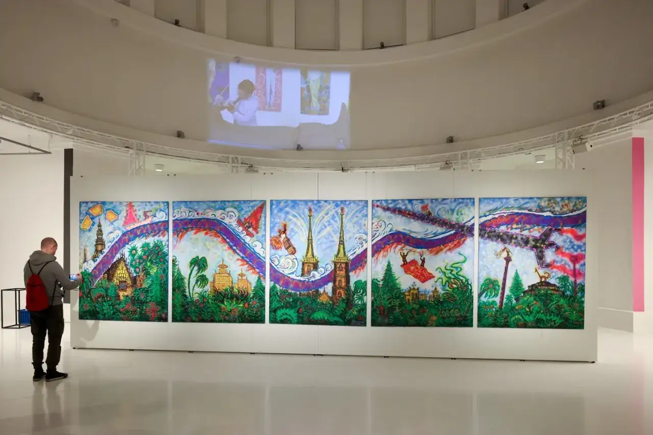 W muzeum sztuki Wrocław mężczyzna ogląda wielopanelowy obraz z fantastycznym krajobrazem i latającymi obiektami.
