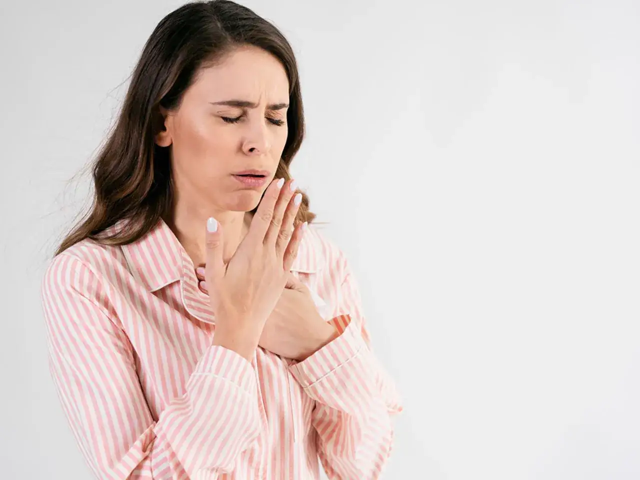 Kobieta w piżamie z r&oacute;żowymi pasami odczuwa silny kaszel, być może związany z refluksem.