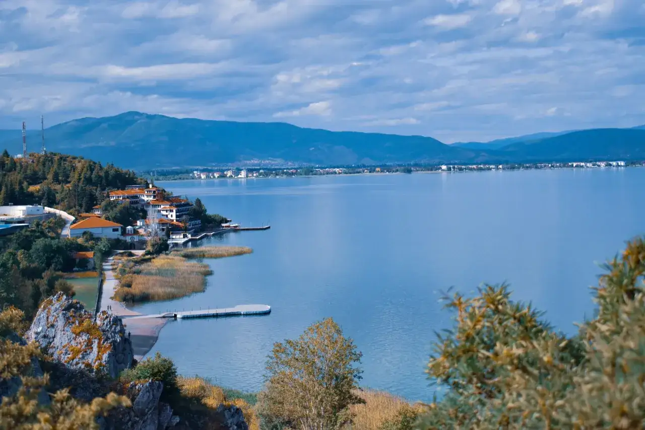 Malownicze jezioro Ochrydzkie z zabudowaniami na wzg&oacute;rzu i g&oacute;rami w tle.