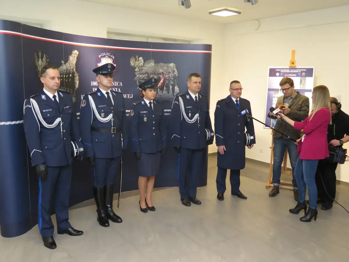 Policjanci w galowych mundurach pozują do zdjęć. Dziennikarka przeprowadza wywiad w sprawie umundurowania policjantów.