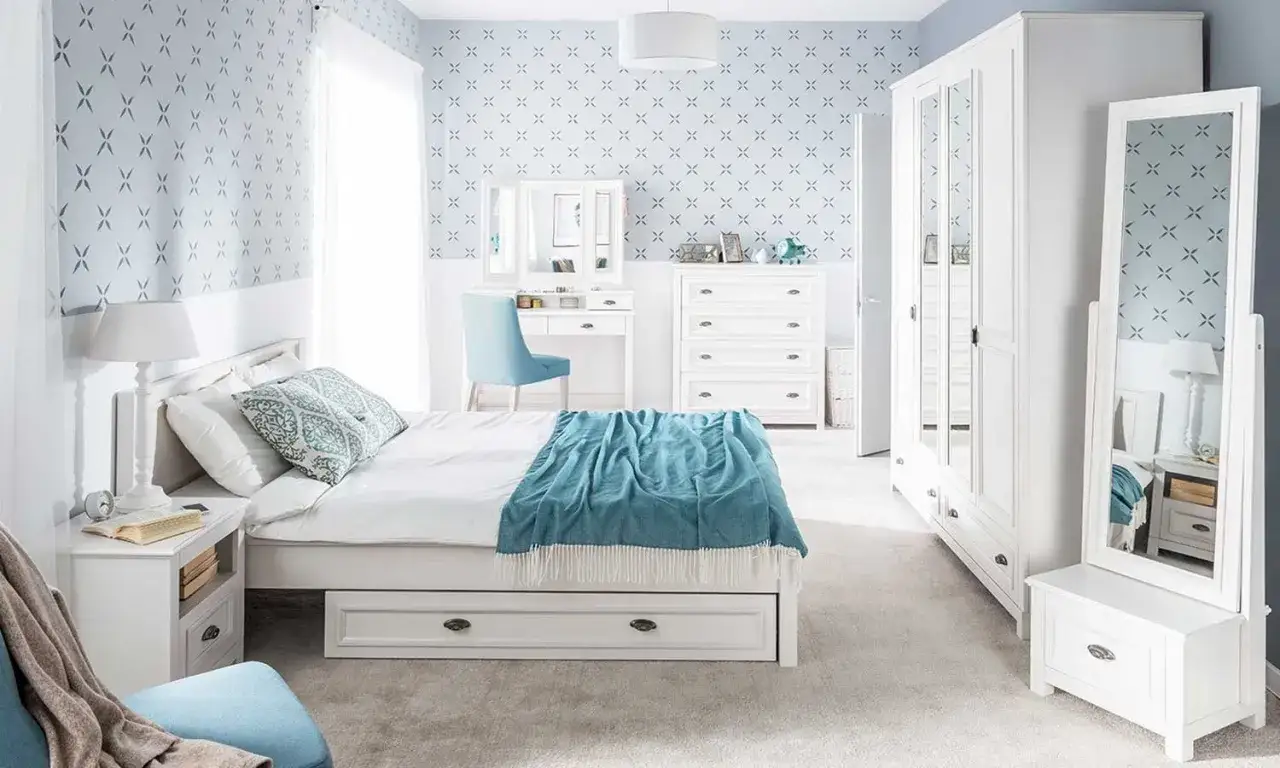 Sypialnia z białymi meblami i tapetą w niebieskie krzyżyki. Jasne ściany i dywan tworzą przytulną atmosferę.