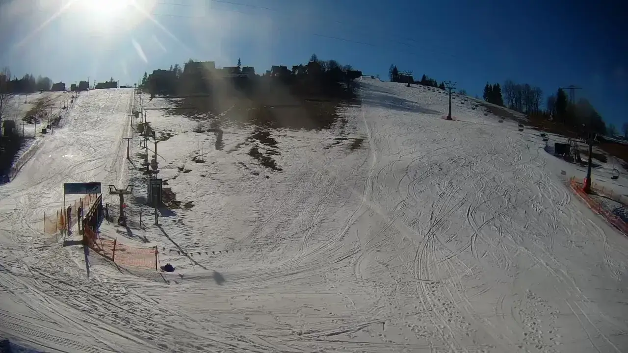 Słoneczny dzień na olczańskim wierchu. Stoki narciarskie z wyciągami i licznymi śladami po nartach.