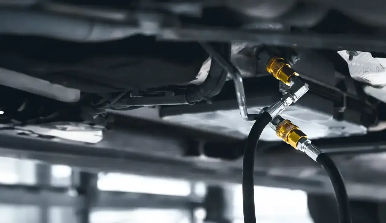 Podwozie samochodu z podłączonymi wężami do statycznej wymiany oleju w automatycznej skrzyni bieg&oacute;w.