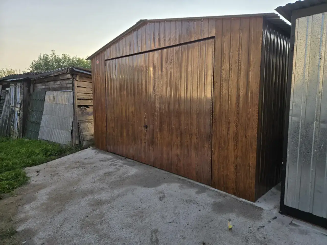 Brązowy garaż blaszany obok drewnianej szopy. Zastanawiasz się, jak pozbyć się wilgoci w garażu blaszanym?