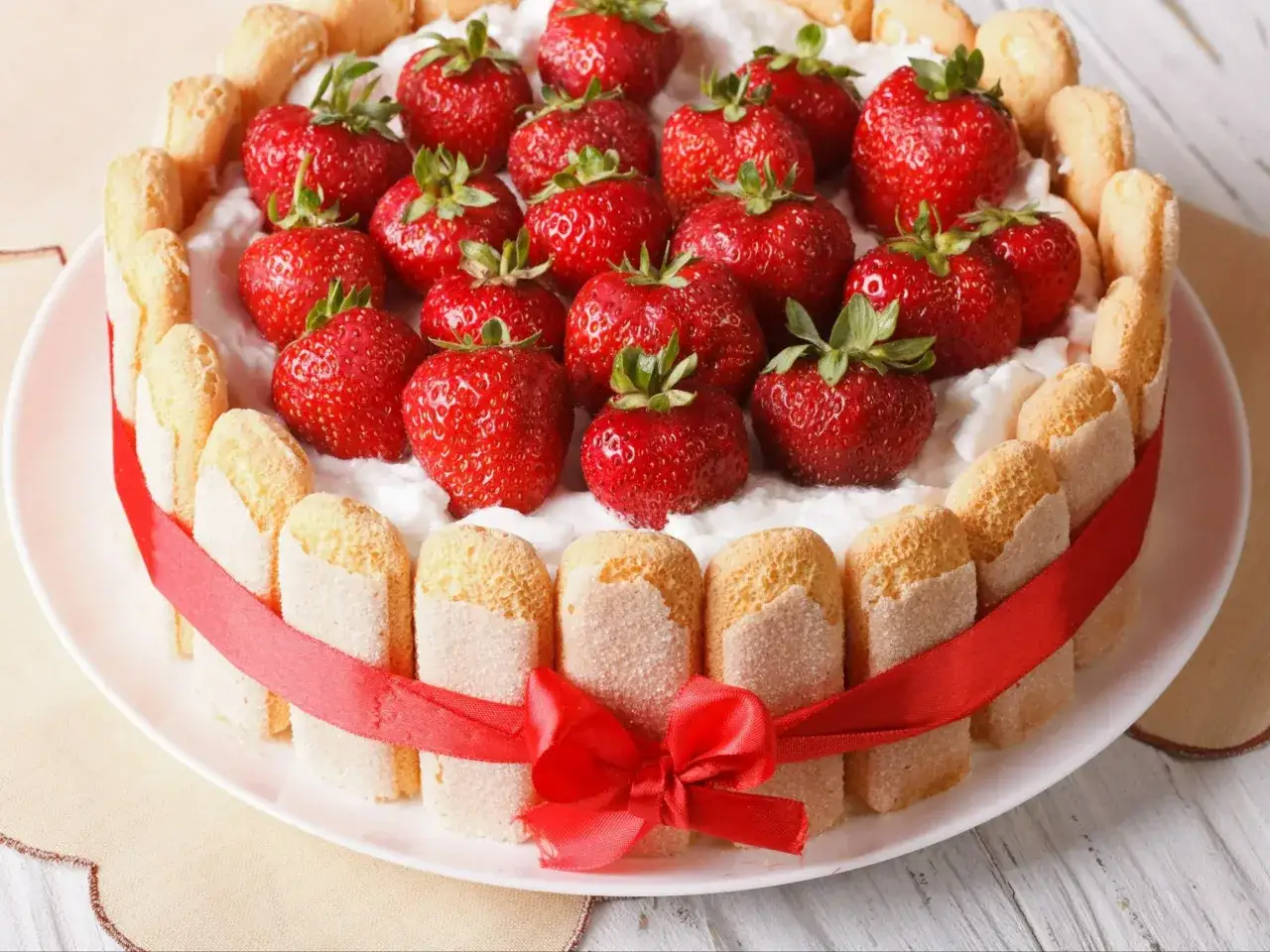 Wykwintne ciasto z biszkoptami, udekorowane świeżymi truskawkami i czerwoną wstążką.