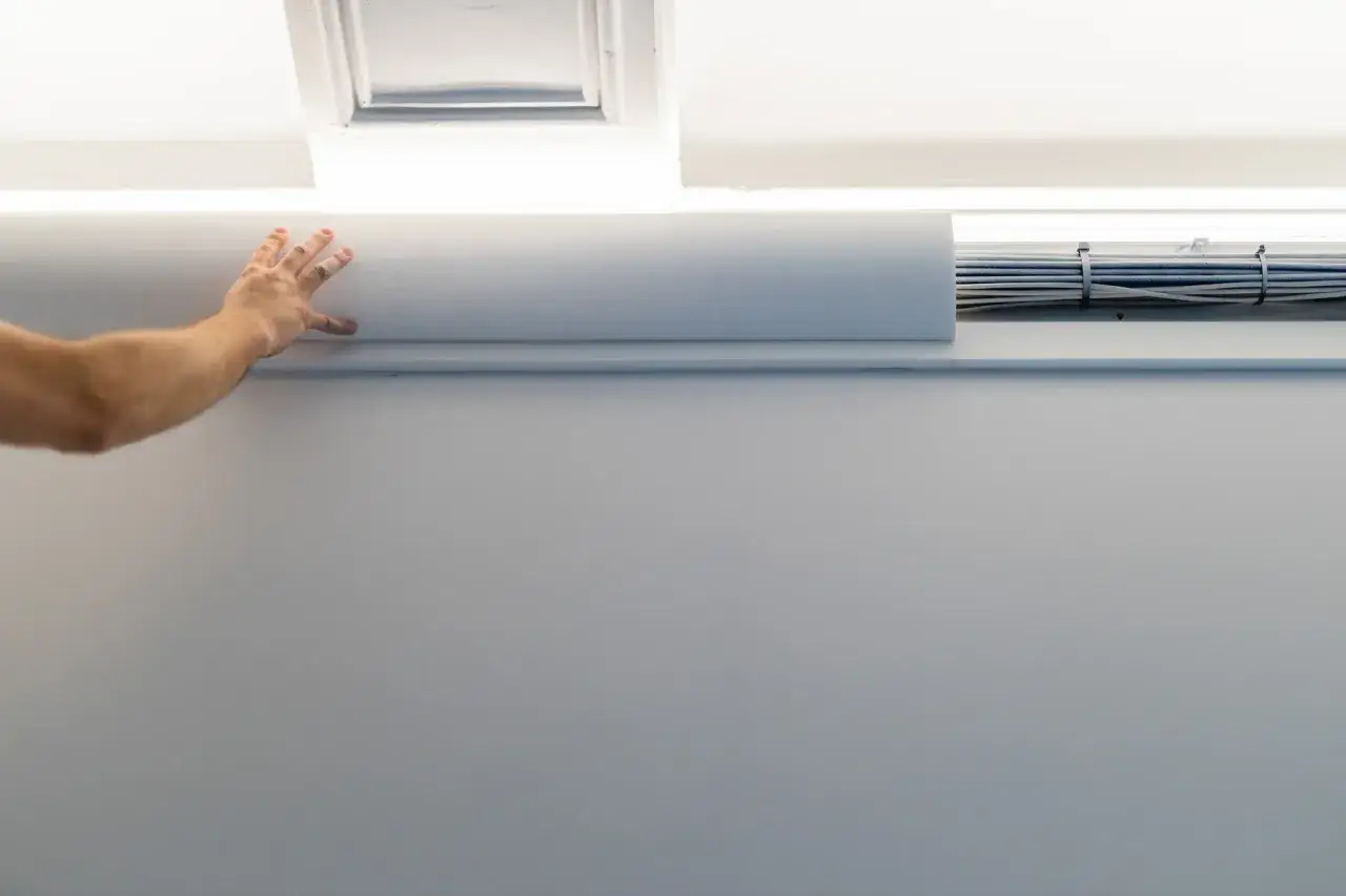 Dłoń przykłada białą listwę maskującą, by jak ukryć wystające kable ze ściany.