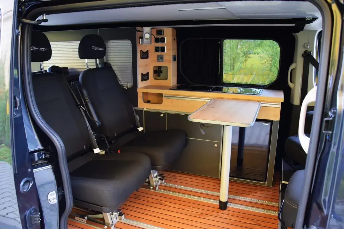 Wnętrze małego vana z dwoma fotelami, aneksem kuchennym, lodówką i rozkładanym stolikiem. Idealny na podróże.