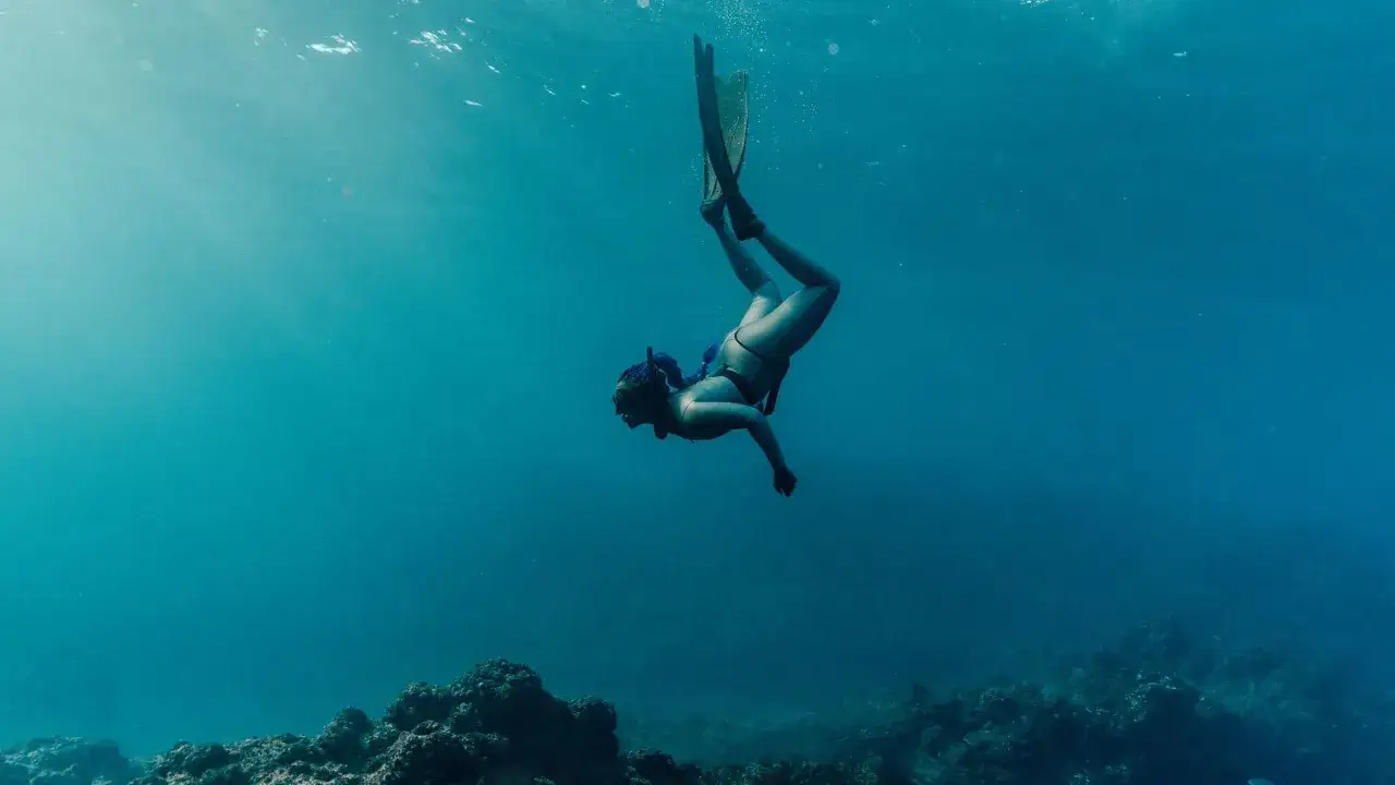 Kobieta nurkuje w turkusowej wodzie, odkrywając jedne z najlepszych miejsc do nurkowania. Podwodny świat kusi.