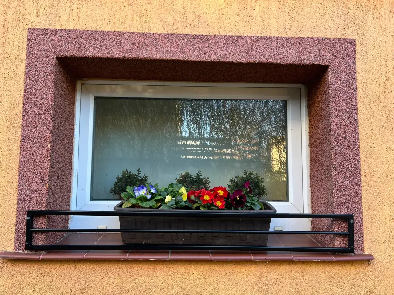 Czarna barierka na parapet bez wiercenia, z doniczką kolorowych kwiatów.