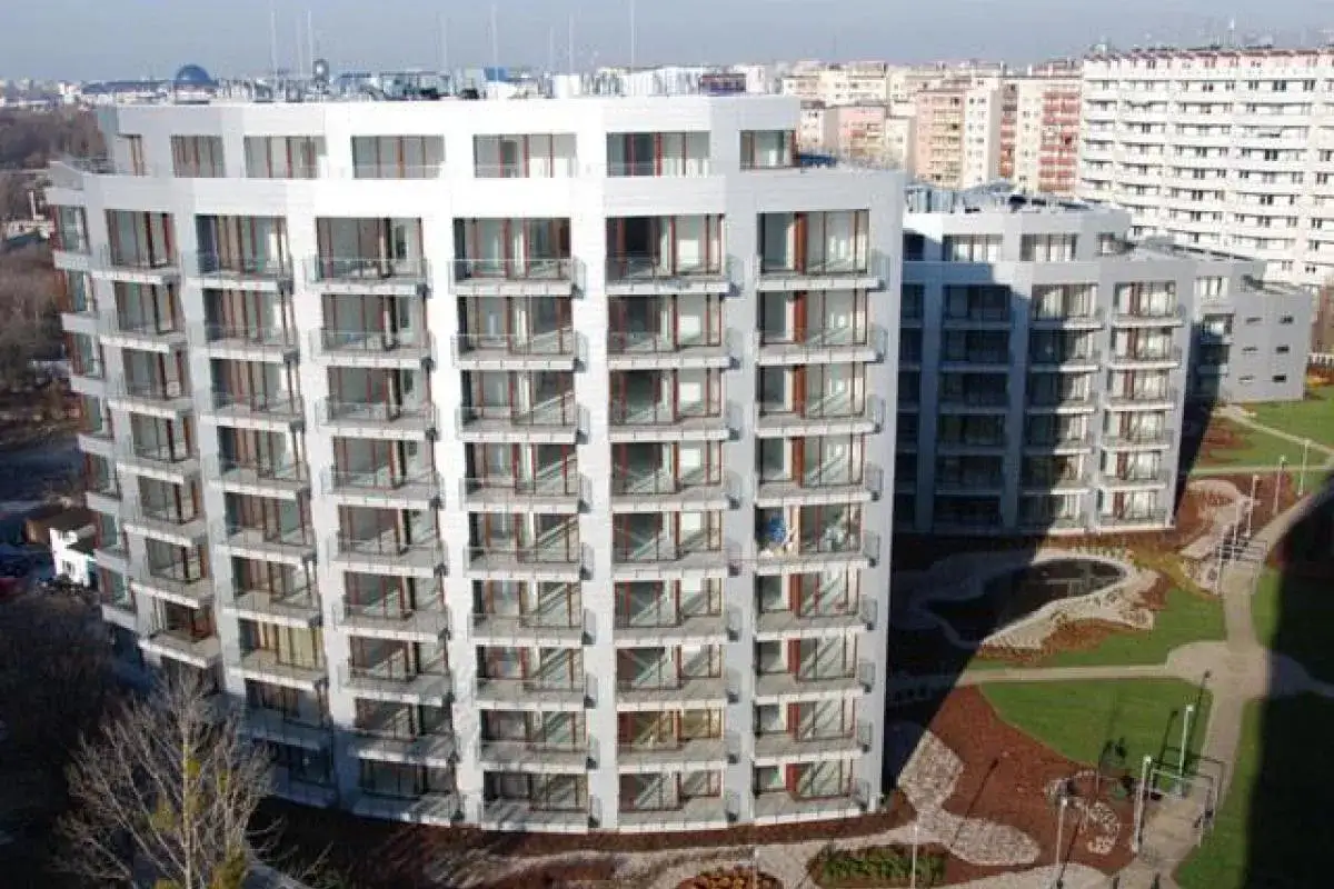 Nowoczesne budynki mieszkalne Triton Park Apartments z balkonami i dużymi oknami, otoczone zielenią i ścieżkami.