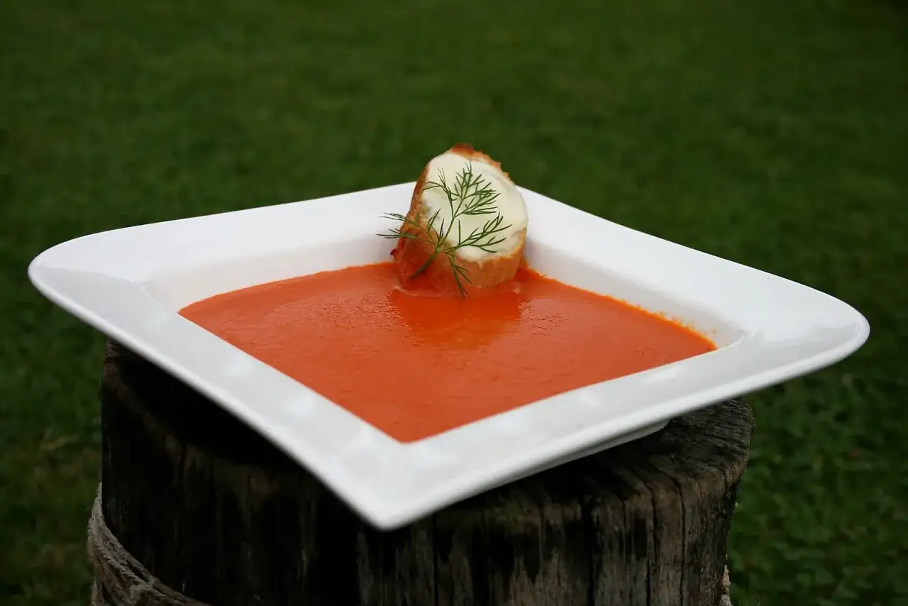 Aksamitny zupa krem z papryki, podana w białej misce, z grzanką i serem.