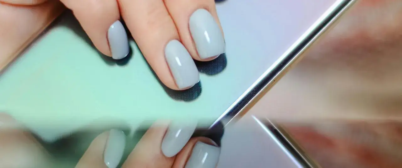 Dłonie z jasnoszarym lakierem hybrydowym na tle lustrzanej powierzchni. Czy hybryda jest szkodliwa?