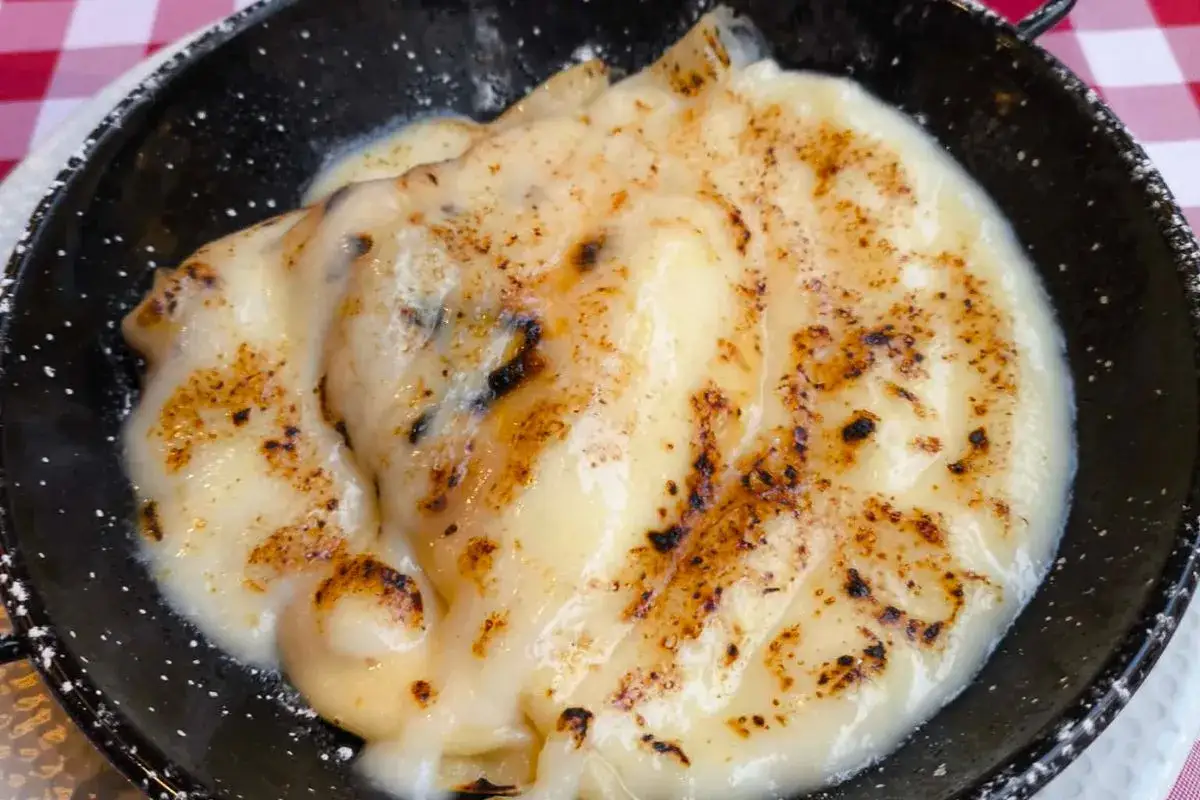 Pyszne naleśniki z serem, zapieczone na złoto, z lekko przypieczonymi brzegami, podane w czarnej patelni.