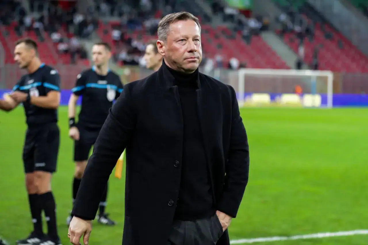 Trener Arki Gdynia na boisku, w tle sędziowie i trybuny. Krążą pogłoski transferowe.